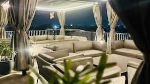 An outdoor seating area with cushioned sofas and chairs, a potted plant, and a view of the city at night. - HOTEL EUPHORIA GREEN (Amritsar)