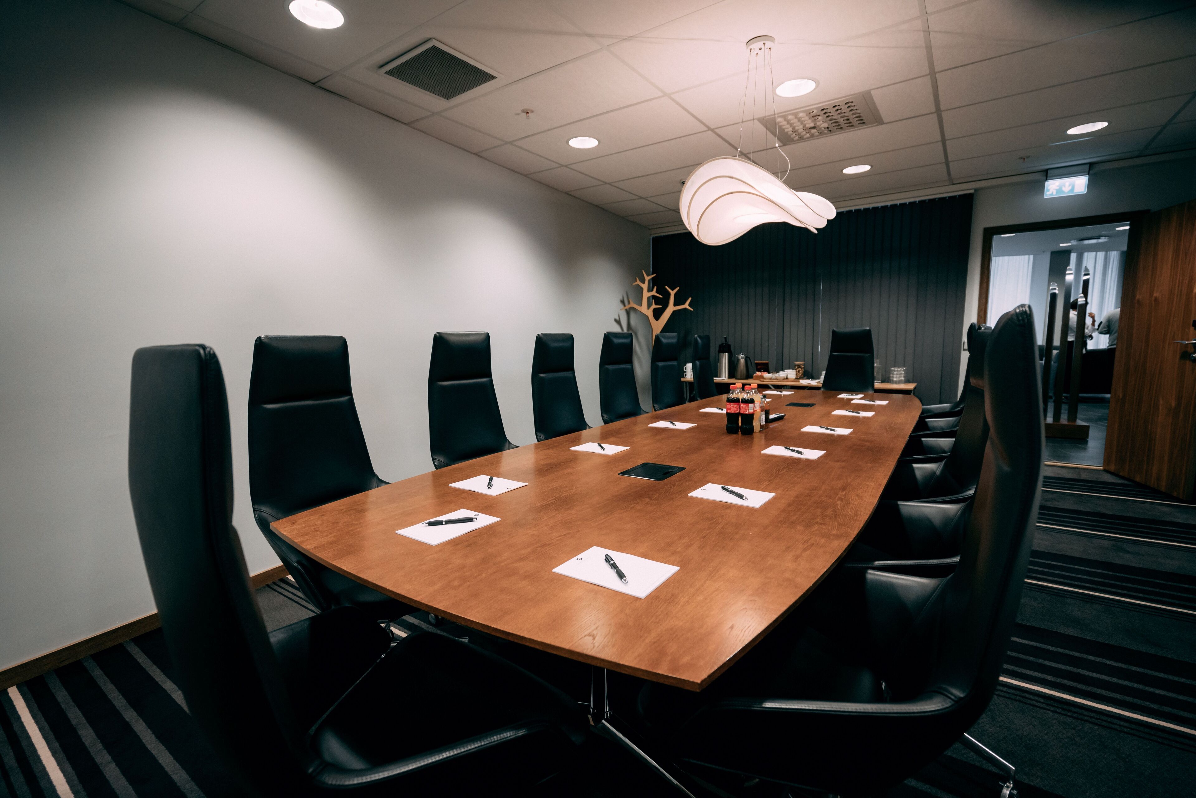 A conference room with a long table, black chairs, and a modern light fixture.