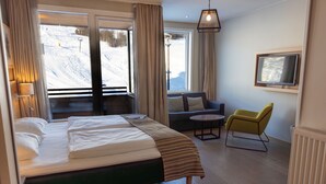 A hotel room with a bed, a sofa, a chair, a TV, and a view of a snowy landscape.