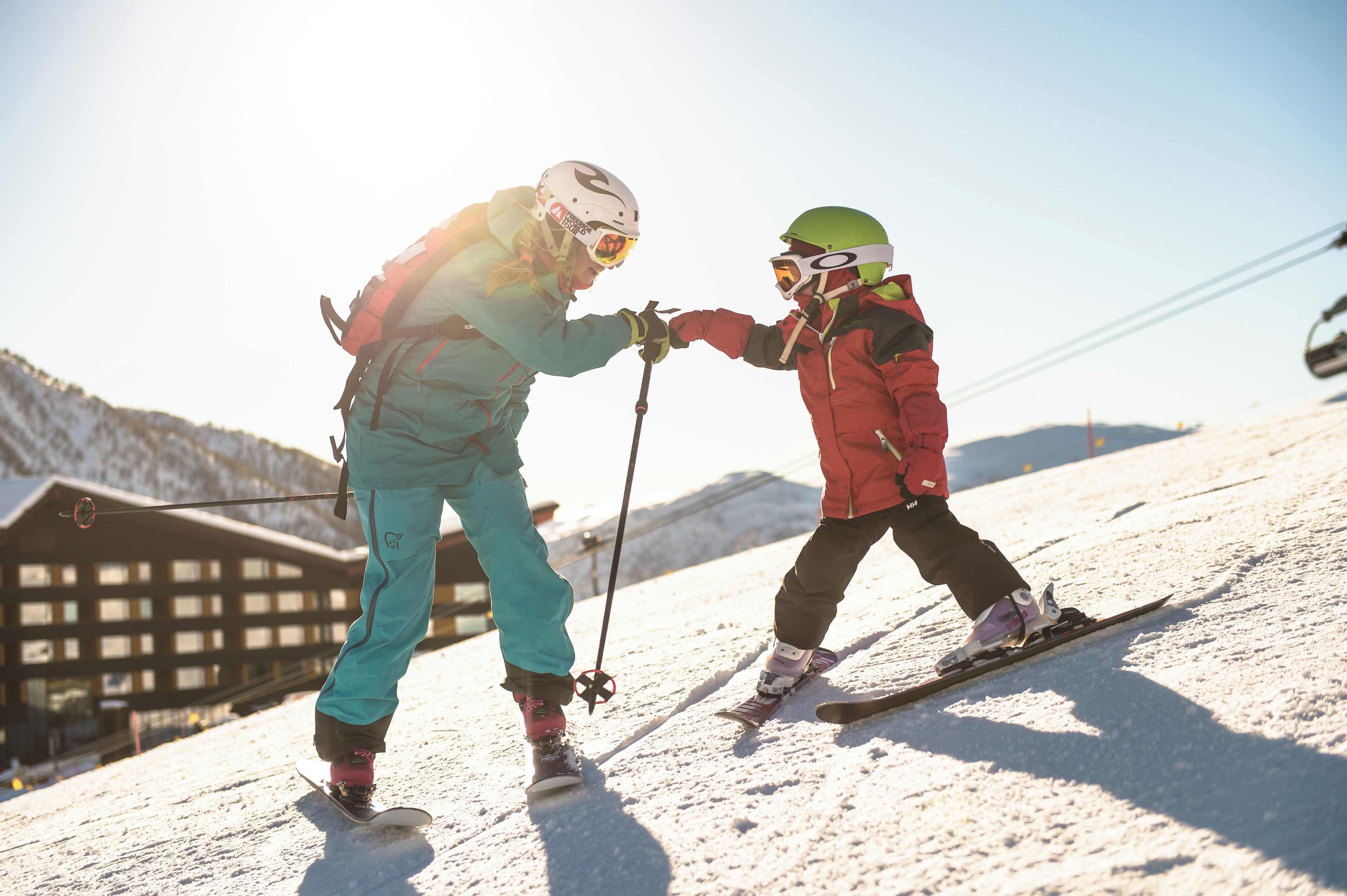 Two skiers on a snowy slope with a wooden cabin in the background.