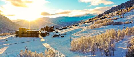 A snow-covered ski resort with buildings, ski lifts, and a mountain backdrop.
