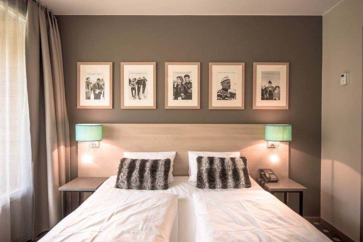 Ein Doppelbett mit zwei Kissen, ein Nachttisch mit Lampe, ein Telefon und gerahmte Bilder an der Wand.