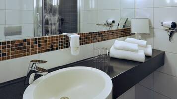 A modern bathroom with a large white sink, a mirror, a shower, and a hairdryer on the counter.