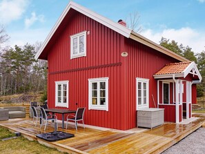 Una casa de madera roja con un porche, un balcón cubierto y una pequeña zona de estar al aire libre con sillas y una mesa.