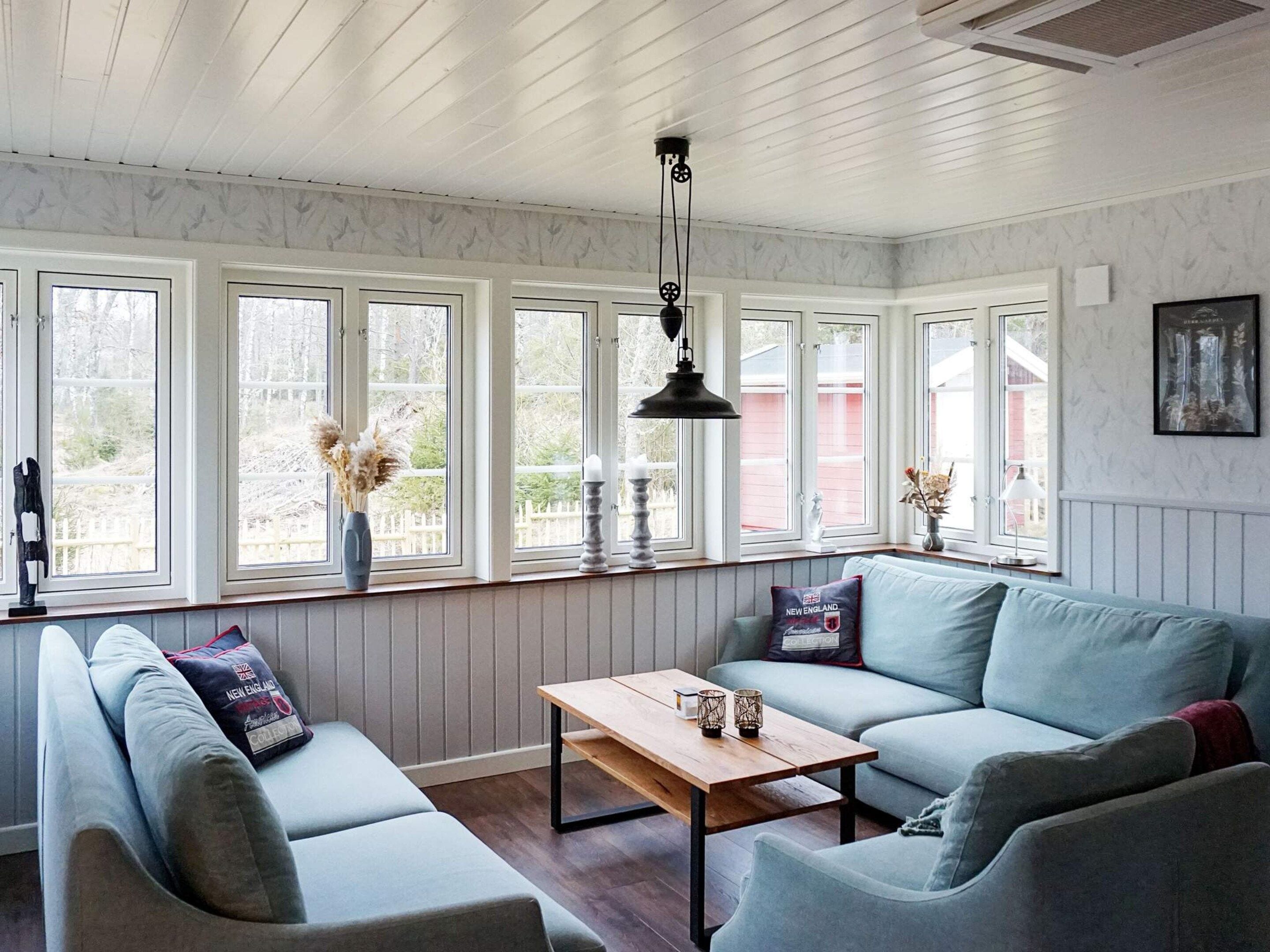 Una habitación con un sofá azul claro, una mesa de madera y un ventanal con vista a un edificio rojo.