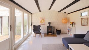 A living room with a fireplace, a sofa, a chair, and a bookshelf. - 4 Person Holiday Home in Jaegerspris (Jægerspris)