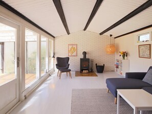 A living room with a fireplace, a sofa, a chair, and a bookshelf. - 4 Person Holiday Home in Jaegerspris (Jægerspris)