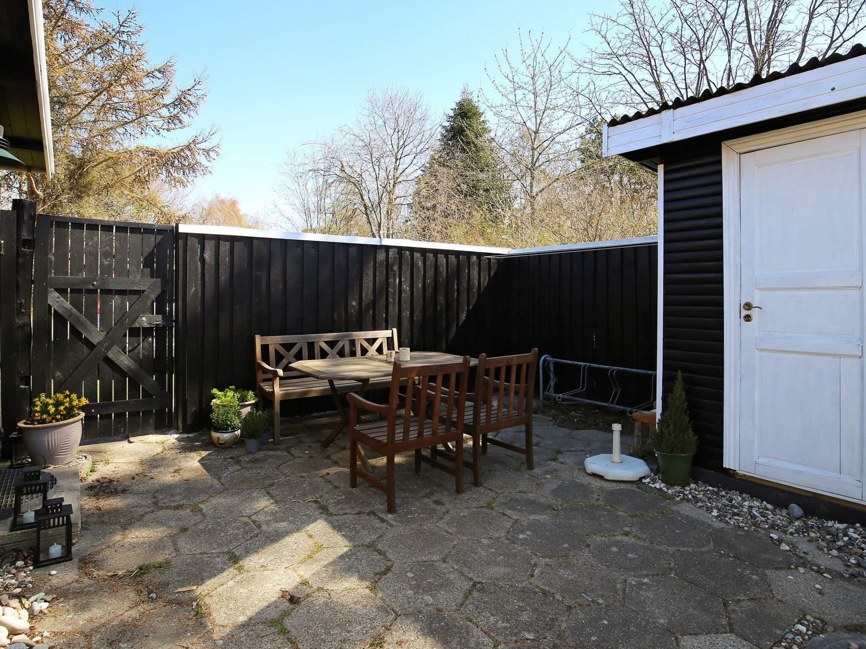 A patio with a wooden table and chairs, a bench, and a white garage door.