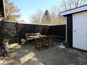 A patio with a wooden table and chairs, a bench, and a white garage door.