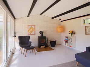 Ett vardagsrum med en tegelvägg, en öppen spis, en svart fåtölj, en soffa och en bokhylla.