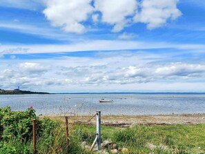 A coastal landscape with a body of water, a boat, and a grassy area with a fence.
