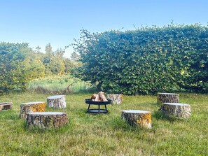 A grassy outdoor area with a fire pit surrounded by tree stumps.