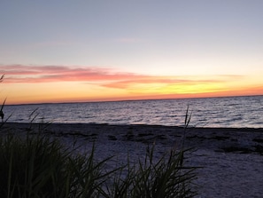 A beach with a sunset, calm sea, and tall grasses in the foreground. - 4 Person Holiday Home in Allingabro (Allingåbro)