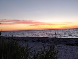 A beach with a sunset, calm sea, and tall grasses in the foreground. - 4 Person Holiday Home in Allingabro (Allingåbro)