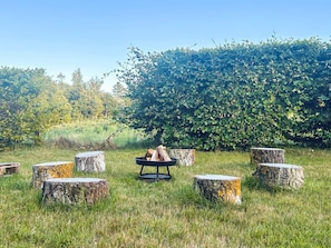 A grassy outdoor area with a fire pit surrounded by tree stumps.