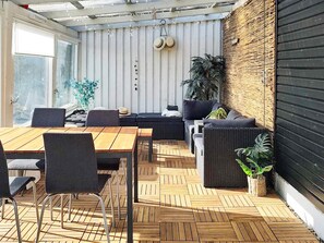 A sunlit patio with a wooden table, chairs, and a seating area with cushions.