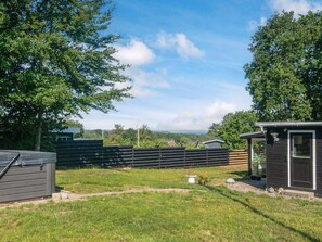 A fenced backyard with a small shed, a grassy lawn, and a view of distant hills. - 4 Person Holiday Home in Allingabro (Allingåbro)