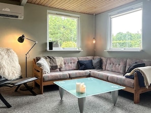 A cozy room with a sectional sofa, a glass coffee table, a lamp, and two windows offering a view of greenery. - 4 Person Holiday Home in Allingabro (Allingåbro)