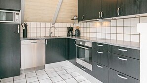 A modern kitchen with dark cabinetry, a built-in microwave, and a coffee maker. - 8 Person Holiday Home in Blavand (Blavand)