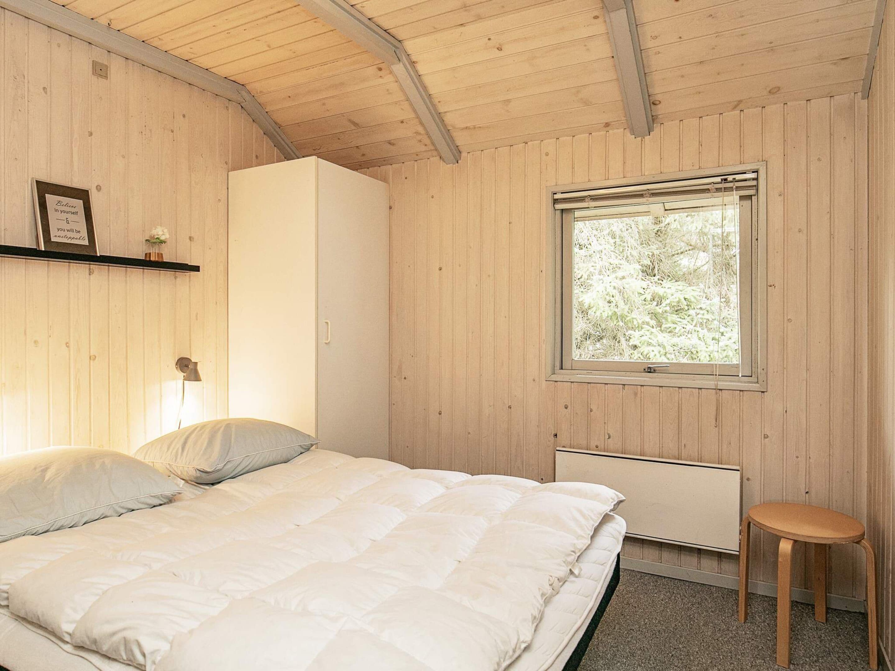 Une chambre à coucher avec un lit, une fenêtre, un radiateur et une étagère sur laquelle est posée une image.