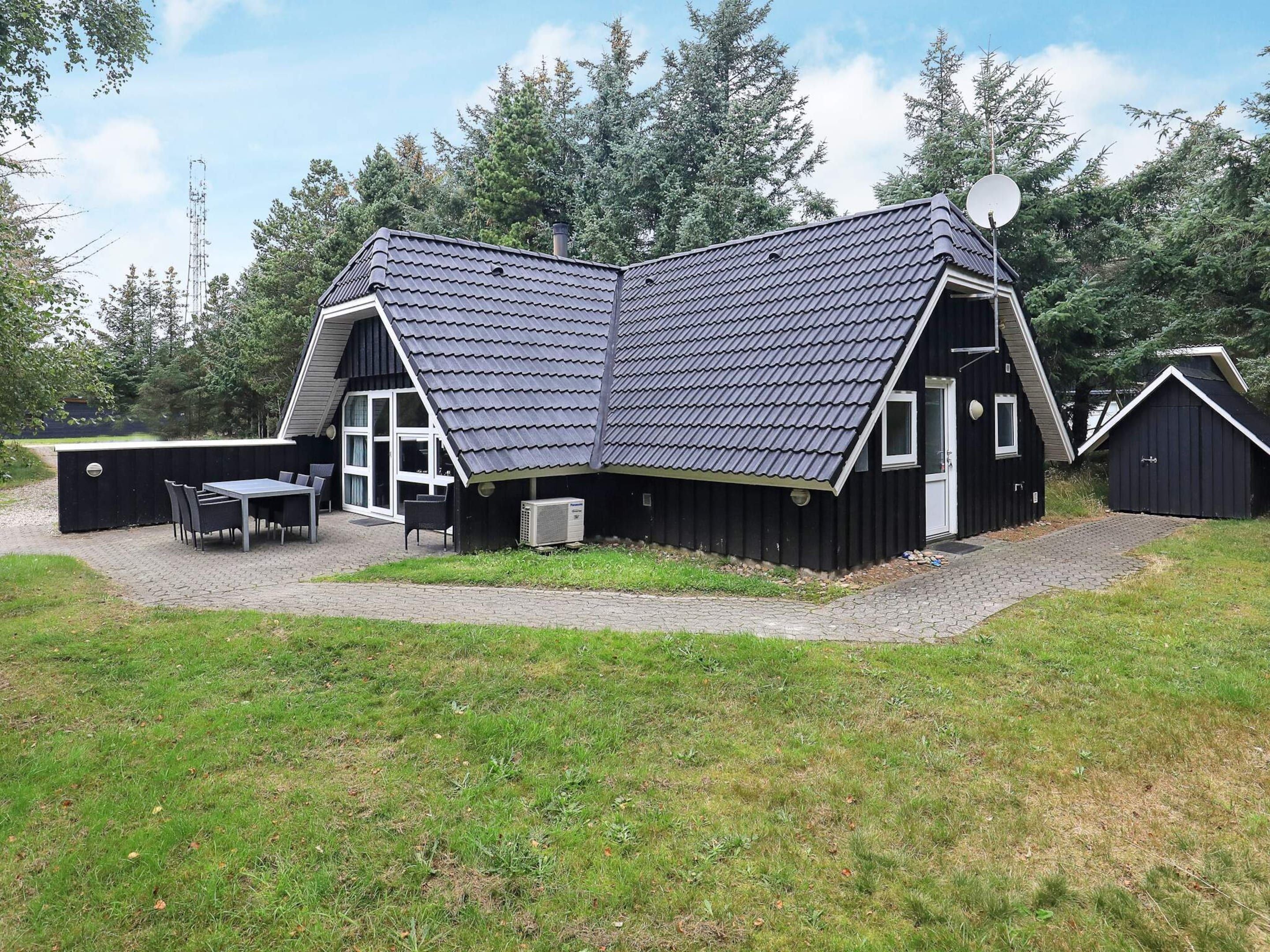 A modern house with a sloped roof, a satellite dish, and a patio with a table and chairs.