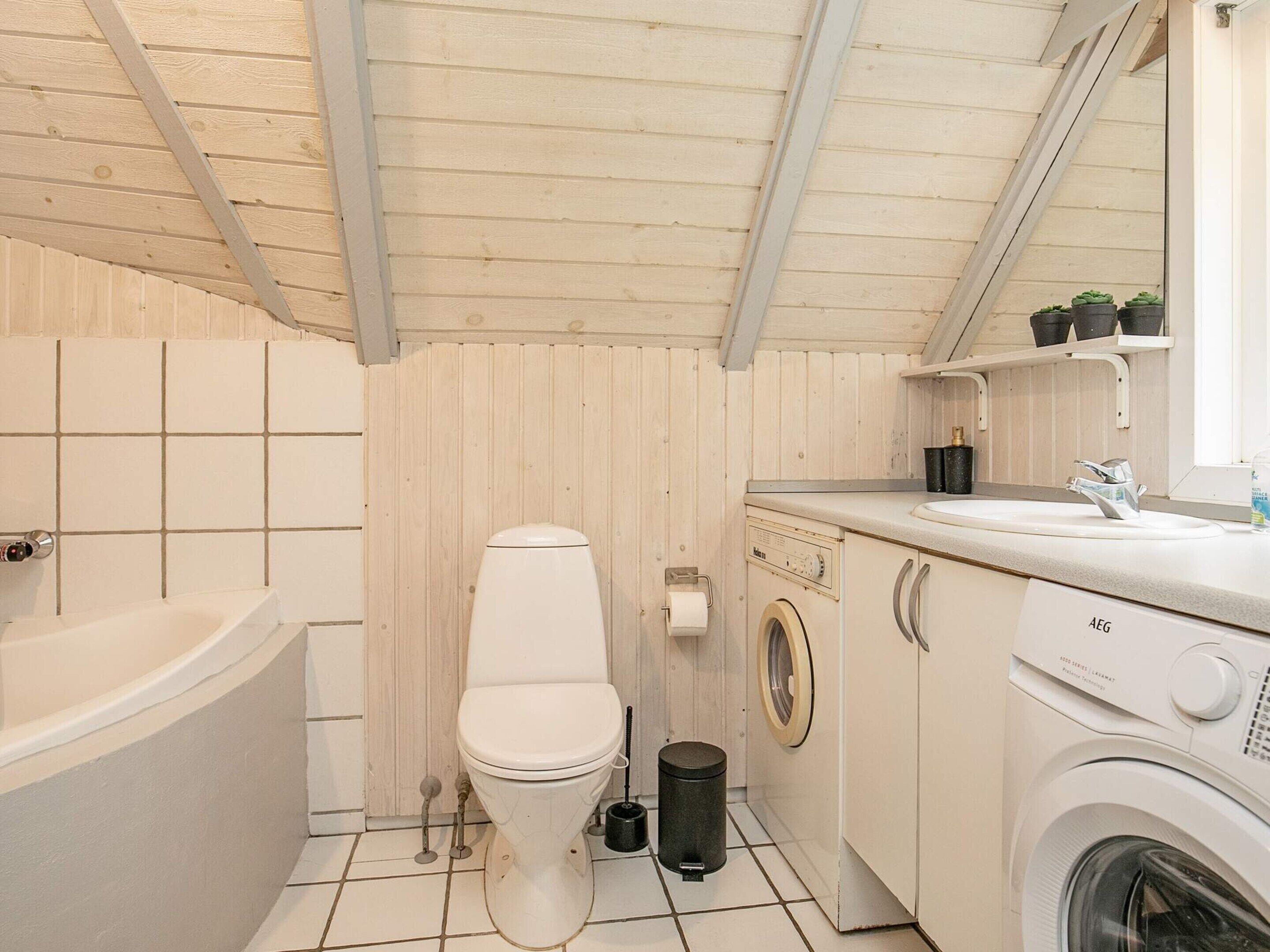 A compact bathroom with a toilet, washing machine, and sink.
