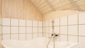 A bathroom with a bathtub, tiled walls, and a wooden ceiling. - 8 Person Holiday Home in Blavand (Blavand)