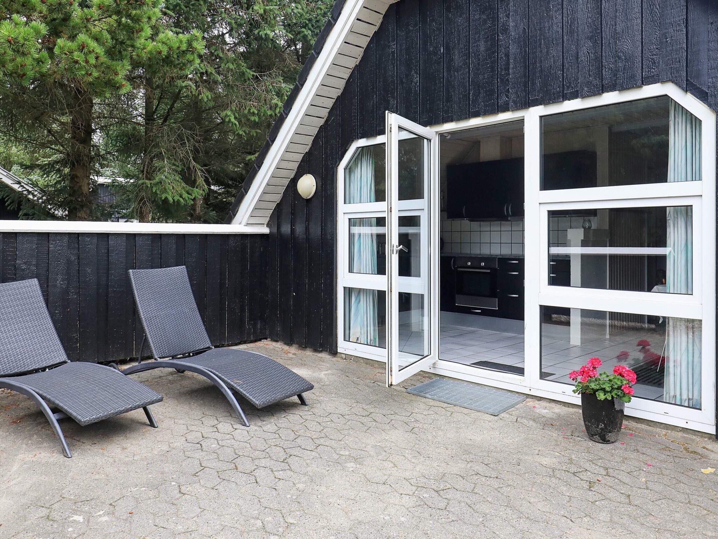 A building with a black exterior, a glass door entrance, and a patio area with two chairs and a potted plant.