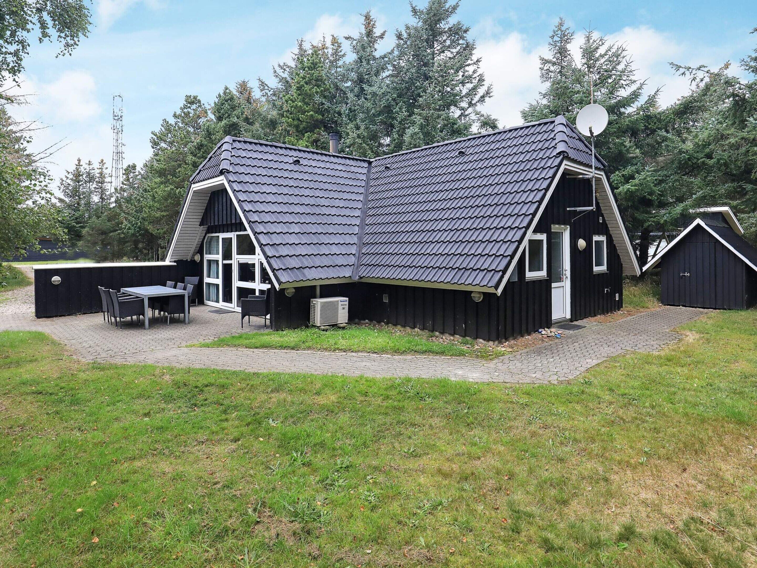 Une maison moderne avec un toit en pente, une antenne parabolique et une terrasse dotée d’une table et de chaises.
