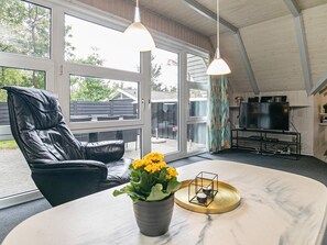 Een moderne woonkamer met een leren fauteuil, een marmeren tafel, een tv-meubel en grote ramen.