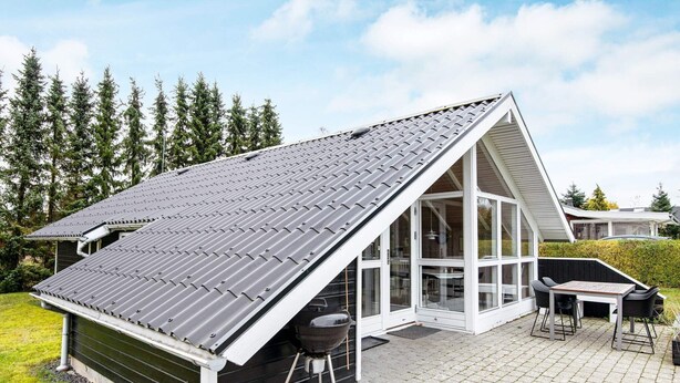 Ett modernt hus med ett sluttande tak, en täckt uteplats med grill och utsikt över den omgivande skogen.