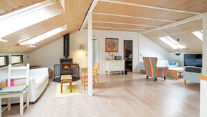A cozy loft bedroom with a sloped ceiling, a built-in wood-burning stove, a bed, a desk, and a TV. - 8 Person Holiday Home in Kirke Hyllinge (Kirke Hyllinge)