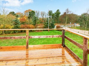 A wooden deck with a metal railing, surrounded by a grassy area and trees.