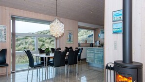 A modern kitchen with a wood-burning stove, a dining area with a table and chairs, and large windows offering a view of the outdoors. - 4 Person Holiday Home in Henne (Henne)