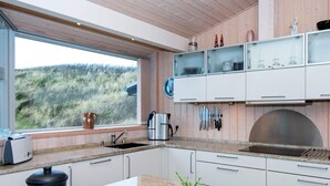 A modern kitchen with white cabinets, a stainless steel sink, and a window overlooking a grassy landscape. - 4 Person Holiday Home in Henne (Henne)