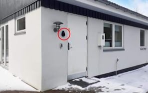 A building with a white exterior, a door with a security camera, and a window.