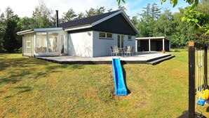 Una casa moderna con porche cubierto, tobogán y patio cercado.