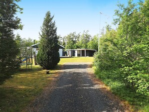 A gravel path leading to a building with a covered porch, surrounded by greenery and trees.
