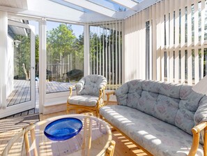 Una habitación iluminada por el sol con un ventanal que da al exterior, una mesa redonda de vidrio y dos sillones tapizados.