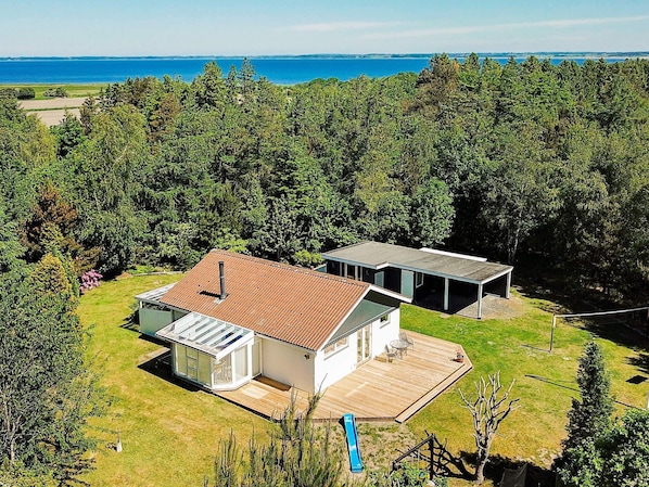 Ett modernt hus i två våningar med en stor terrass, ett inglasat rum och utsikt över havet.