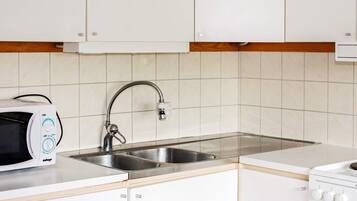 Una cocina con armarios blancos, un lavamanos de acero inoxidable, un microondas y una estufa.