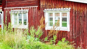 Un bâtiment en bois rouge, doté de deux fenêtres et entouré de verdure.