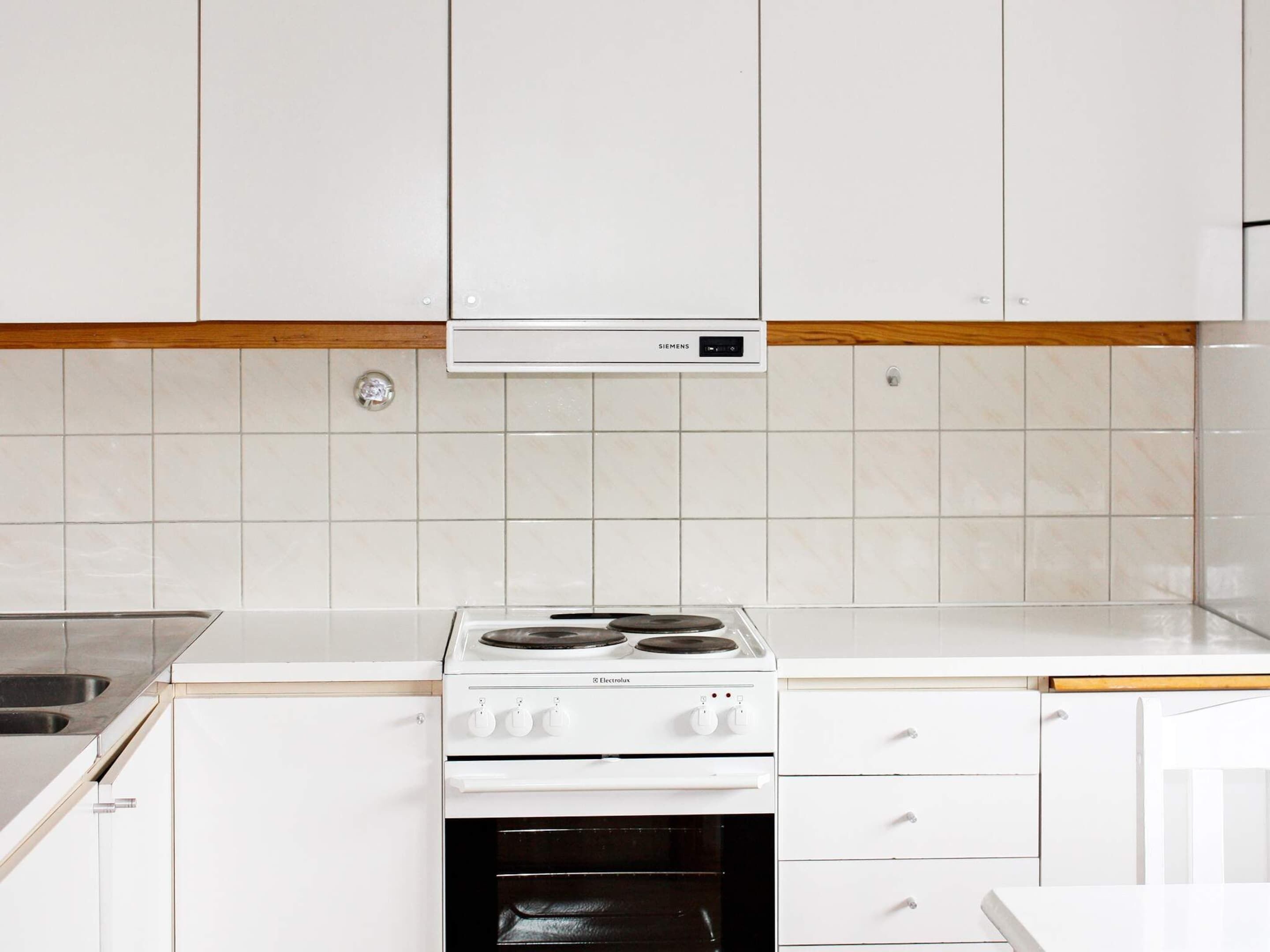 A kitchen with white cabinets, a white countertop, a Siemens range hood, and a white Electrolux stove.