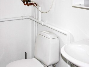 Un water bianco con serbatoio, un lavandino bianco e un impianto idraulico a vista.
