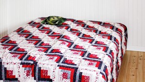 A bed with a quilt featuring a geometric pattern and a pillow with a cat design. - 4 Person Holiday Home in Tallberg (Tallberg)