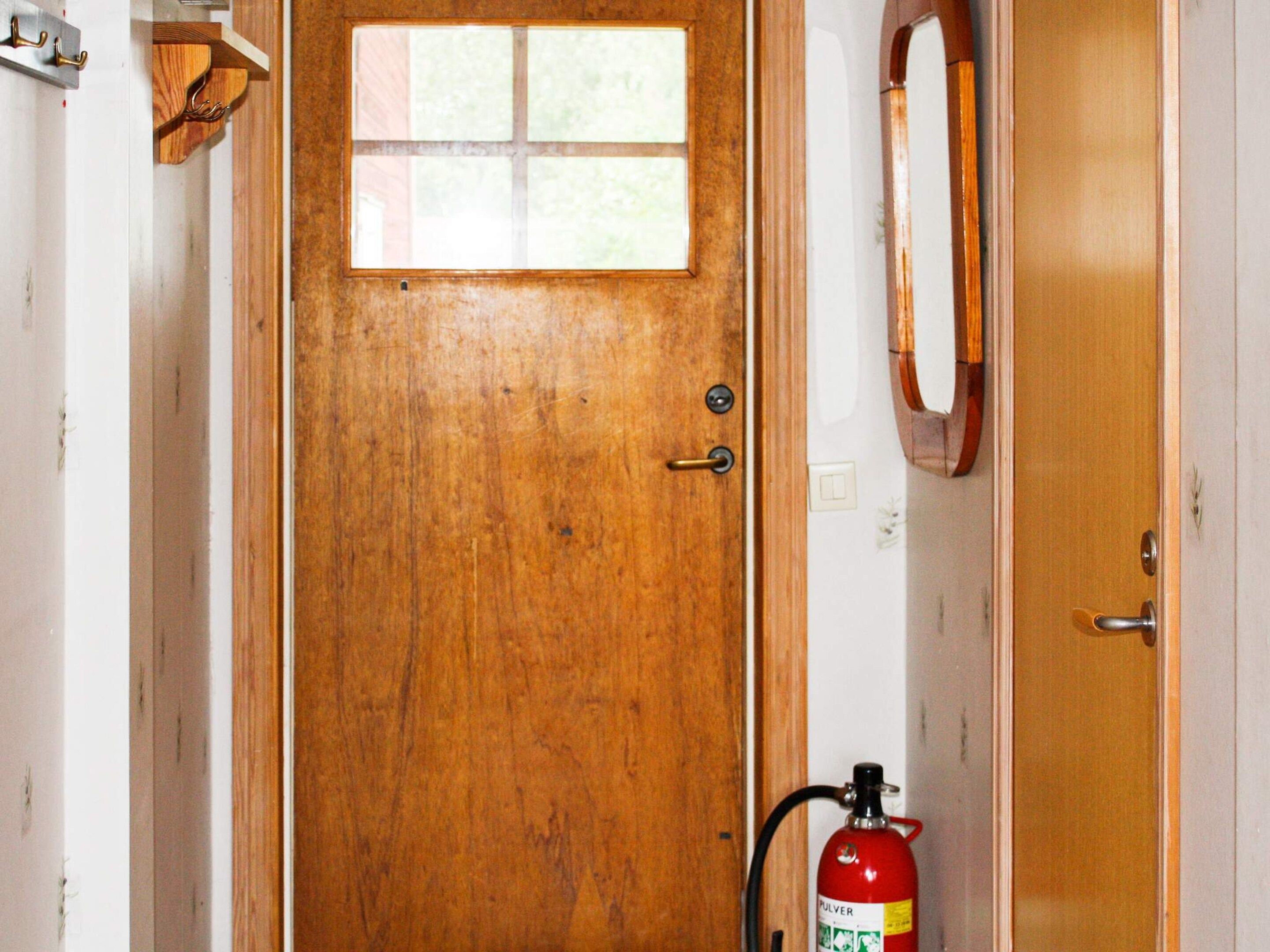 Une porte en bois avec une fenêtre, un extincteur et un miroir accroché au mur.