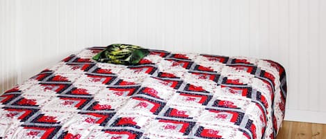 A bed with a patterned quilt, a pillow, and a wooden floor.