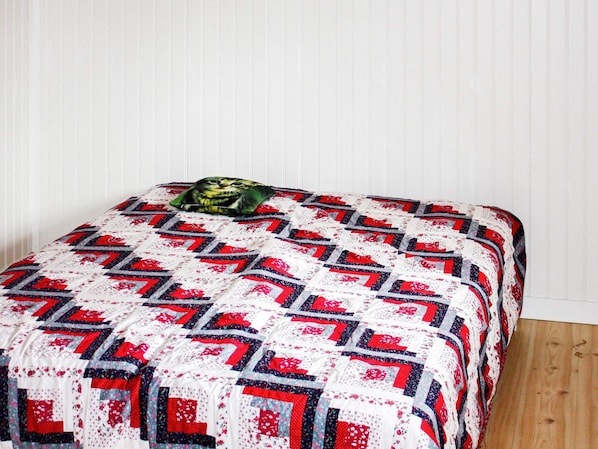 Uma cama com colcha estampada, um travesseiro e piso de madeira.