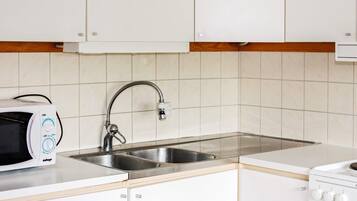 A kitchen with white cabinets, a stainless steel sink, a microwave, and a stove.