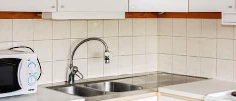 Una cocina con gabinetes blancos, un lavamanos de acero inoxidable, un microondas y una estufa.
